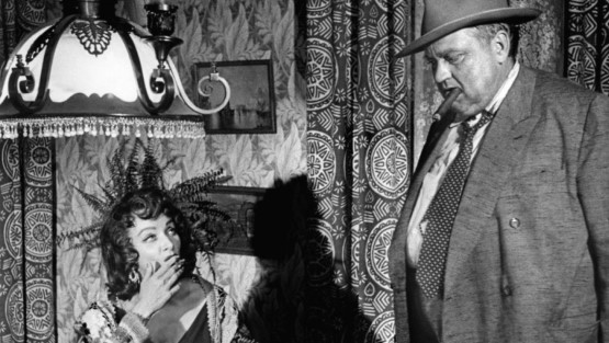 Marlene Dietrich fumando mira a un hombre gordo con un puro en la boca.