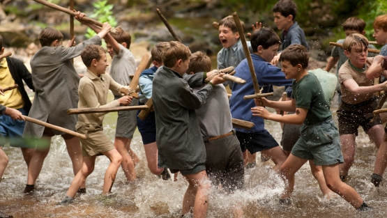 Un grupo de niños pelean con palos en un río.